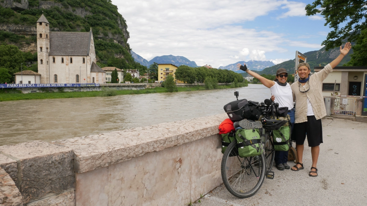 Annie and Ge with open arms in front of a River In Trento, Italy